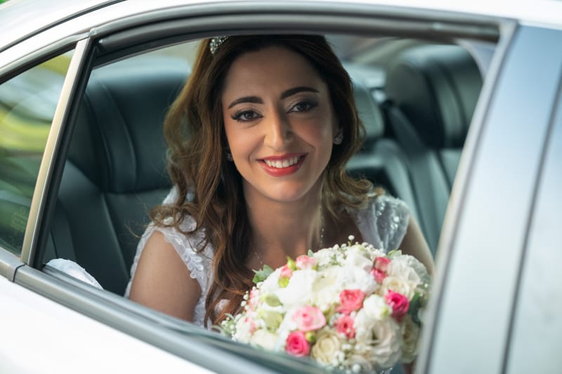 Noiva sorrindo pela janela do carro, com o buquê no colo