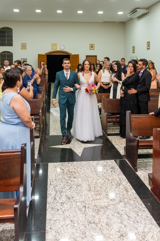 Noivos saindo de mãos dadas pelo corredor da igreja, entre os convidados
