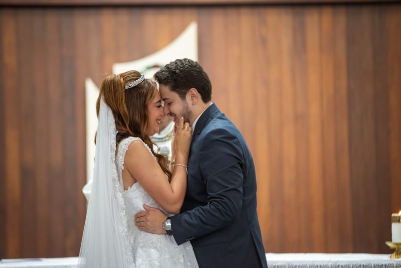 Noivos de testa colada no altar, de olhos fechados