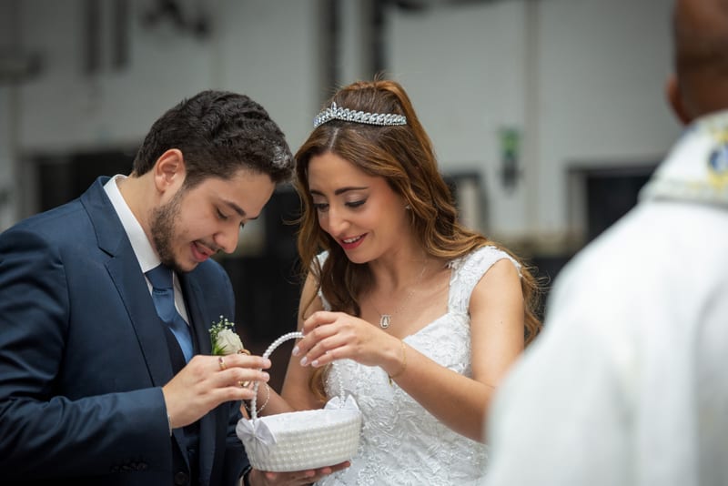 Noivos sorrindo ao pegar as alianças na cestinha