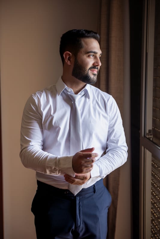 Noivo ajustando o punho da camisa perto da janela