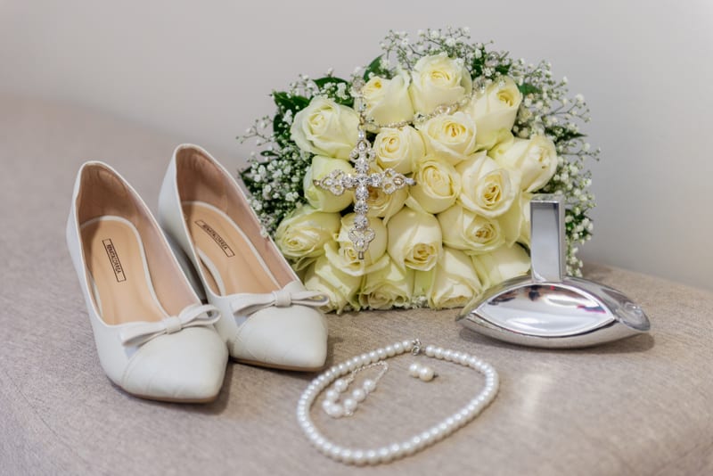 Sapatos, buquê de rosas brancas, terço e colar de pérolas