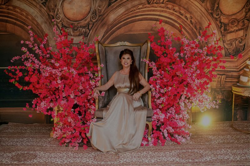 Aniversariante sentada diante de um painel de flores vermelhas